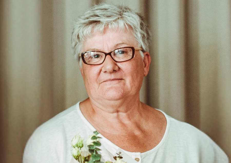 Zdjęcie portretowe. Na zdjęciu starsza kobieta w krótkich siwych włosach i okularach. Lekko się uśmiecha. Z tyłu jasne tło.