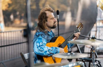 W parku Szczęśliwickim na scenie siedzi mężczyzna i gra na gitarze