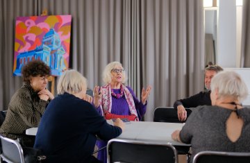 grupa seniorów siedząca przy stole, opowiadająca sobie ciekawe historie.