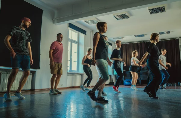 Zdjęcie przedstawia uczestników naśladujących instruktorkę, która uczy ich stepować