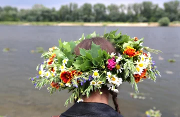 zdjęcie przedstawia kobietę patrzącą na rzekę. Na głowie ma wianek z kolorowych kwiatów
