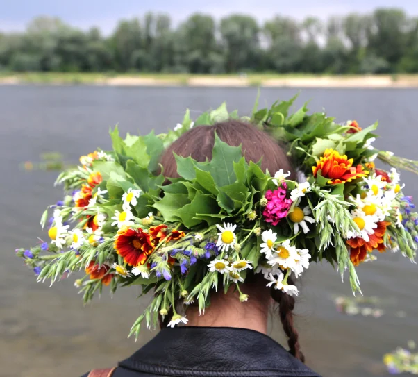 zdjęcie przedstawia kobietę patrzącą na rzekę. Na głowie ma wianek z kolorowych kwiatów