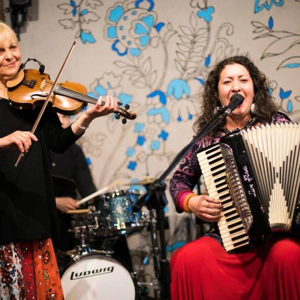 zdjęcie przedstawia dwie kobiety. Jedna stoi i gra na skrzypcach, druga siedzi i gra na akordeonie
