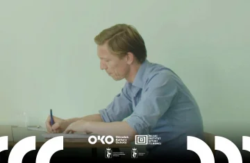 Zdjęcie przedstawia mężczyznę siedzącego przy biurku i prawą ręką wypełnia dokument