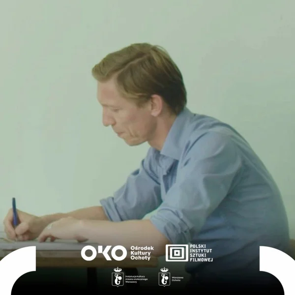 Zdjęcie przedstawia mężczyznę siedzącego przy biurku i prawą ręką wypełnia dokument