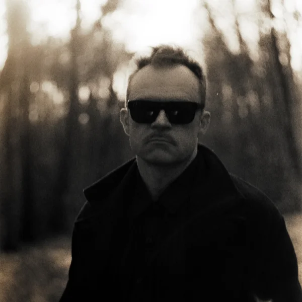 zdjęcie przedstawia artystę. Mężczyzna pozuje do zdjęcia na tle lasu