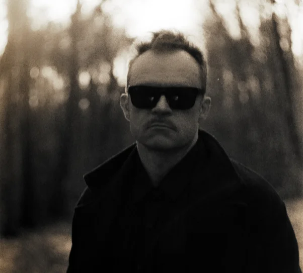 zdjęcie przedstawia artystę. Mężczyzna pozuje do zdjęcia na tle lasu