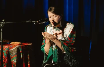 zdjęcie przedstawia artystkę na scenie, ubraną w ludowy strój, śpiewającą do mikrofonu