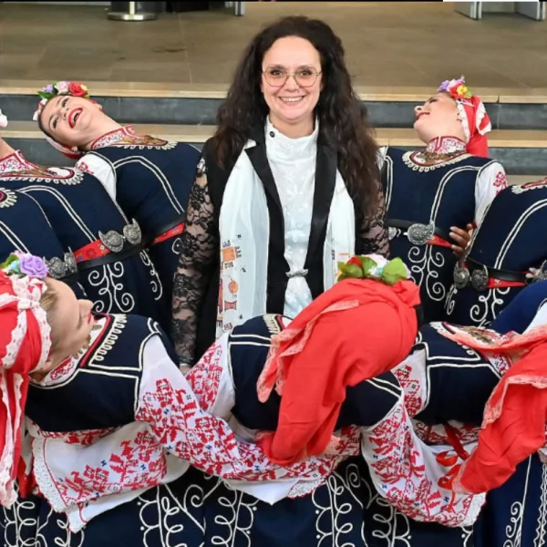 zdjęcie przedstawia kobietę w długich włosach otoczoną kobietami w strojach ludowych z Bułgarii