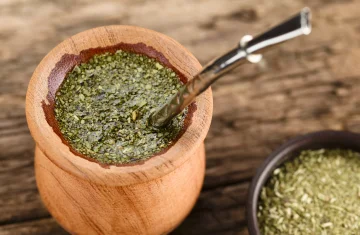A wooden gourd filled with green yerba mate infusion and a metal straw called a bombilla, placed on a wooden table.