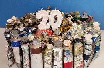 Zdjęcie przedstawia tort zrobiony z tubek farby. Tort ma świeczki z numerem 20, świeczki nie są zapalone. Tort na niebiesko-białym tle.