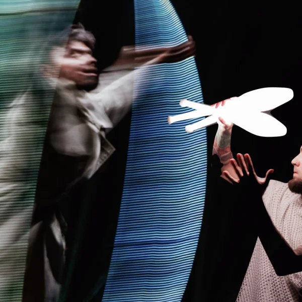 Artysta wykonuje dynamiczną akrobację w kole cyrkowym (Cyr wheel), tworząc świetlne smugi na ciemnej scenie.