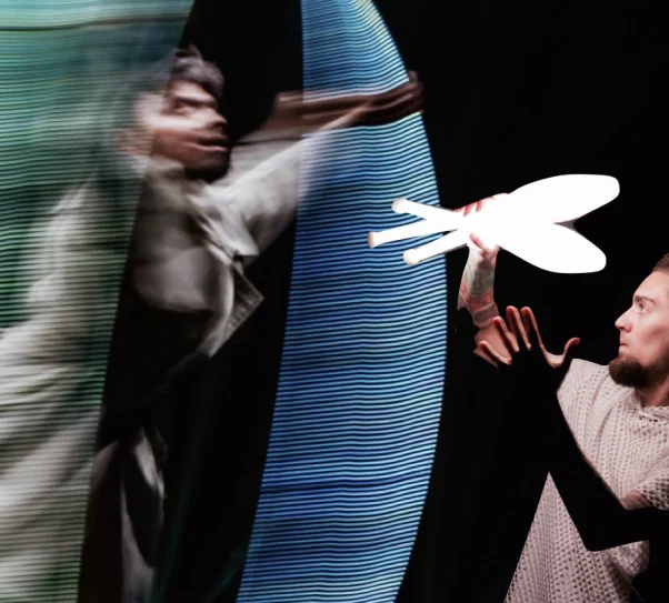 Artysta wykonuje dynamiczną akrobację w kole cyrkowym (Cyr wheel), tworząc świetlne smugi na ciemnej scenie.