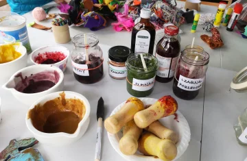 zdjęcie przedstawia przybory malarskie (pojemniczki w farbami, pędzel, słoiczki) na stole