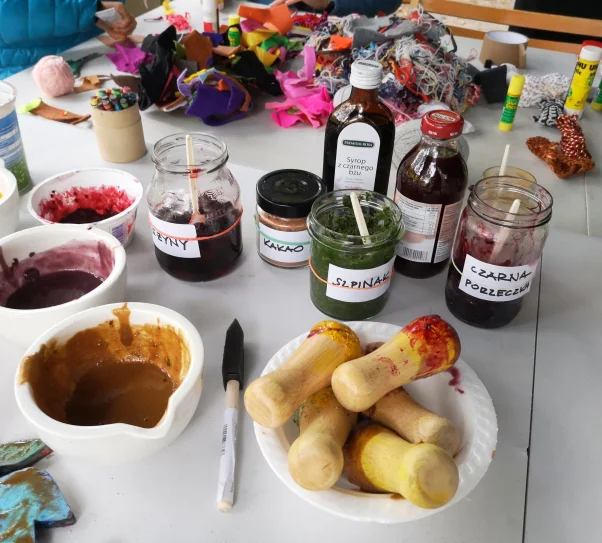 zdjęcie przedstawia przybory malarskie (pojemniczki w farbami, pędzel, słoiczki) na stole