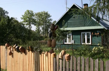 zdjęcie przed zielonym domem, na płocie powieszono dzbanki