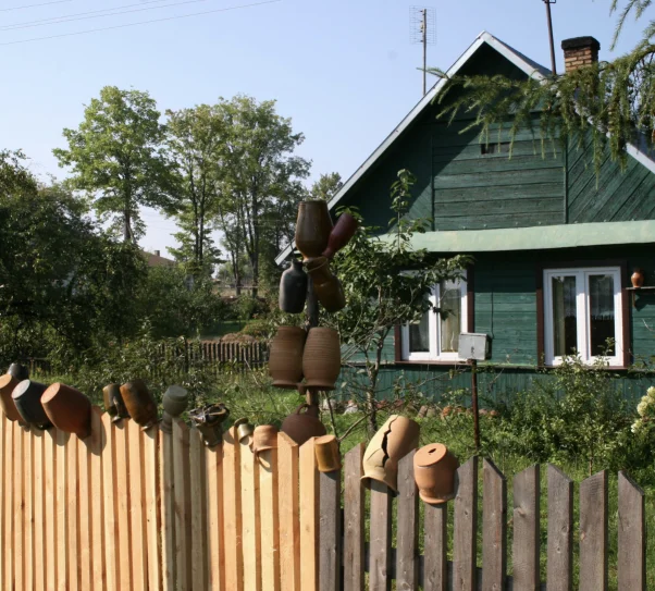zdjęcie przed zielonym domem, na płocie powieszono dzbanki