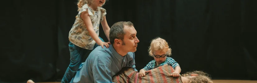 zdjęcie przedstawia rodzinę bawiącą się na podłodze. Dwoje dzieci oraz rodzice.